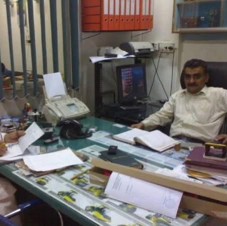 Muhammad Shahzad working at his desk in the early Shahzad Brothers office, survey instruments laid out in the glass counter in front of him